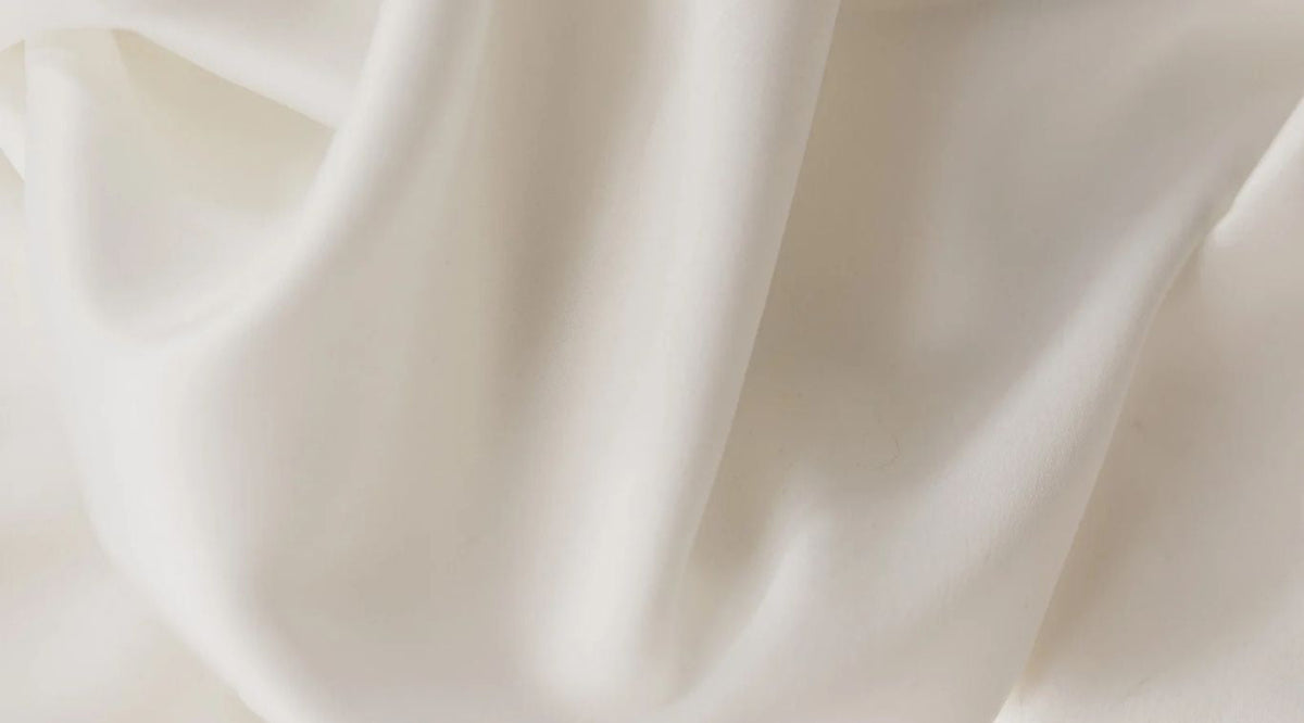 Mykt, hvitt silkestoff i lette folder — bakgrunn for SKADI WEAR